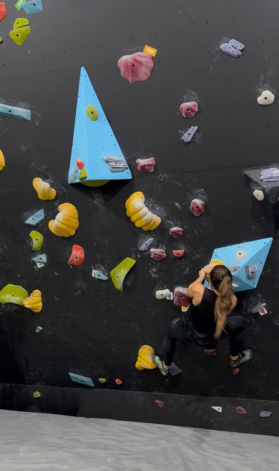 Paola escalando em parede de boulder indoor