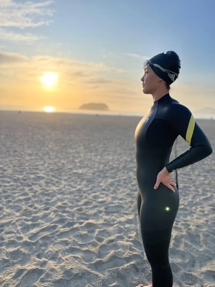 Paola de roupa de neoprene na praia ao nascer do sol